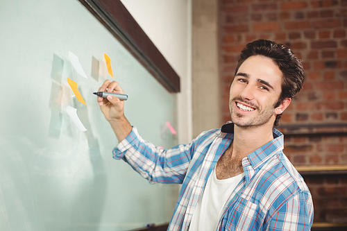 Portrait of smiling businessman holding marker while standing in creative office