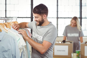 Happy man choosing clothes for donation with woman man in background