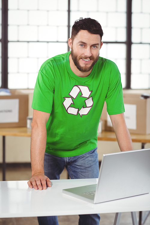 Portrait of man in recycling symbol tshirt working on laptop in creative office
