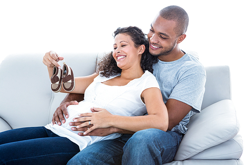 Cheerful young couple with baby shoes sitting on sofa at home