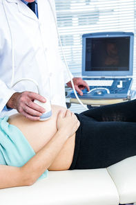 Midsection of doctor performing ultrasound on pregnant woman in clinic