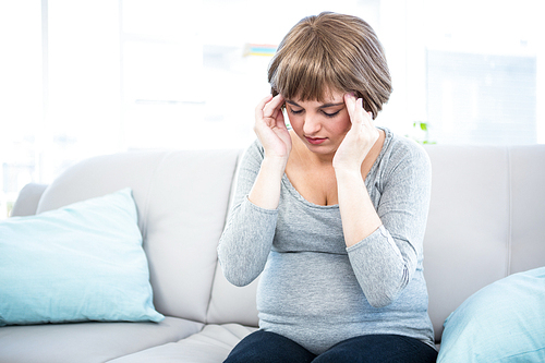 Pregnant woman having headache on couch at home in living room
