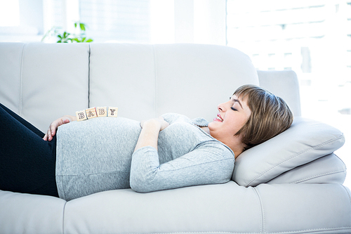 Pregnant woman playing with wooden blocks while lying on a sofa at home