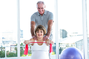 Happy pregnant woman exercising with resistance band while therapist massaging at health club