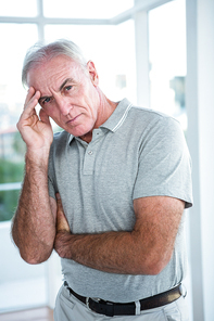 Portrait of tensed man touching his head while standing against window