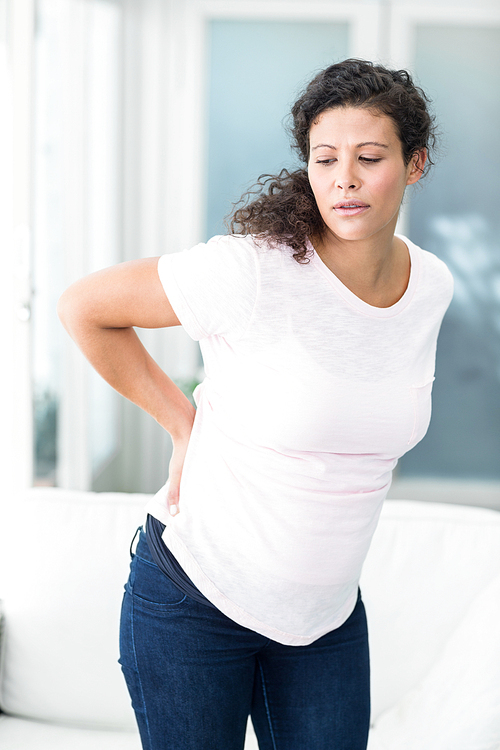 Woman with back pain standing by sofa