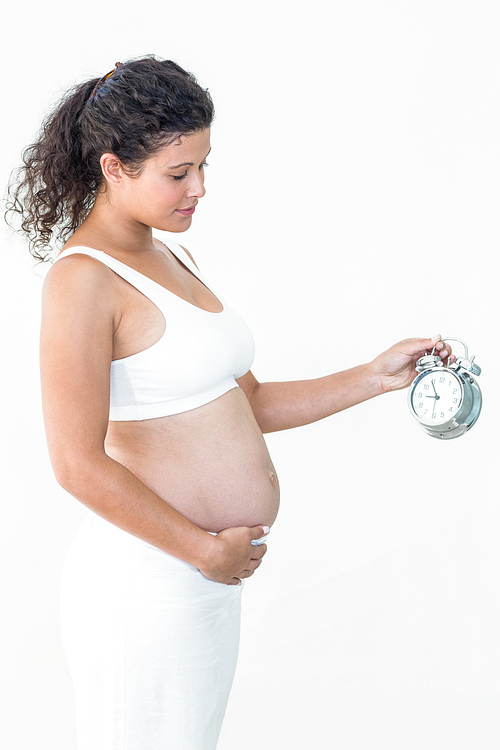 Pregnant woman looking at alarm clock while touching belly