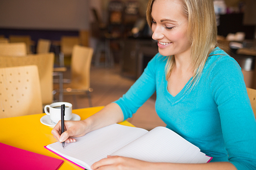 Young woman smiling while writing on book