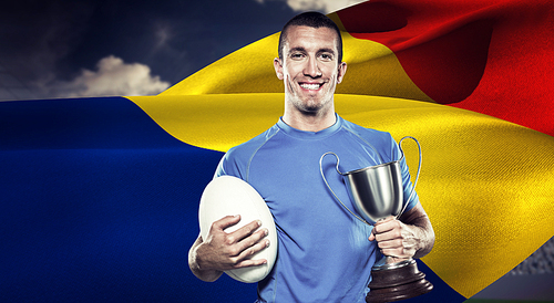 Composite image of portrait of smiling rugby player holding trophy and ball