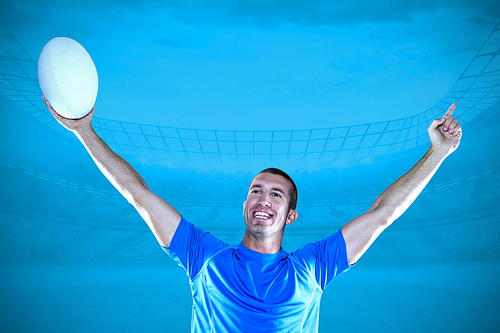 Composite image of happy rugby player in blue jersey holding ball with arms raised