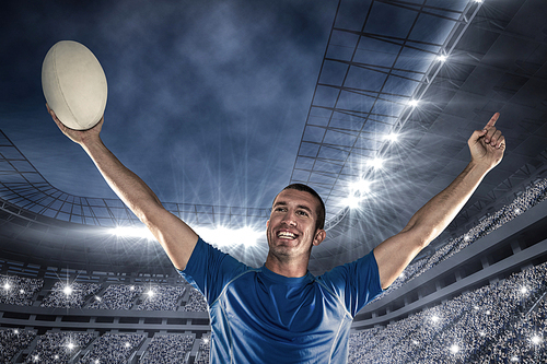 Composite image of happy rugby player in blue jersey holding ball with arms raised