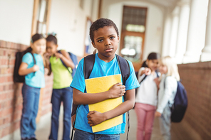 Portrait of sad pupil being bullied by classmates at corridor in school