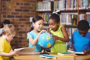 Surprised pupils studying globe in the library in school