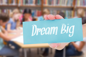 The word dream big and hand showing card against cute pupils writing at desk in library