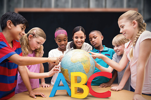 Cute pupils and teacher looking at globe in library  against blackboard with copy space on wooden board