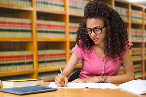 Student sitting in library writing against close up of a bookshelf