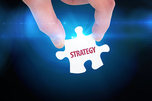 The word strategy  and hand holding jigsaw piece against blue background with vignette