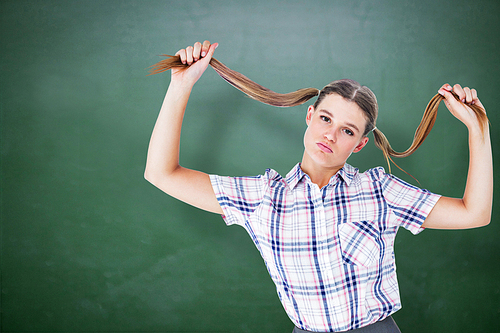 Geeky hipster holding her pigtails against green chalkboard