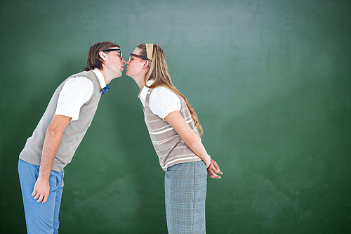 Geeky hipster couple kissing against green chalkboard