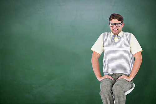 Geeky hipster sitting on stool against green chalkboard