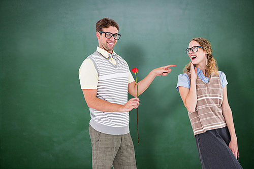 Geeky hipster holding rose and pointing his girlfriend  against green chalkboard