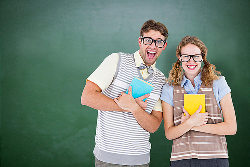 geeky hipster couple holding books and smiling at camera  against green chalkboard