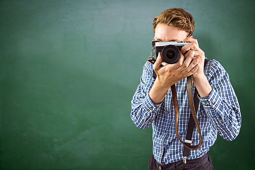 Geeky hipster holding a retro camera against green chalkboard