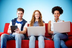 Young adults using electronic devices on couch  against blue background with vignette