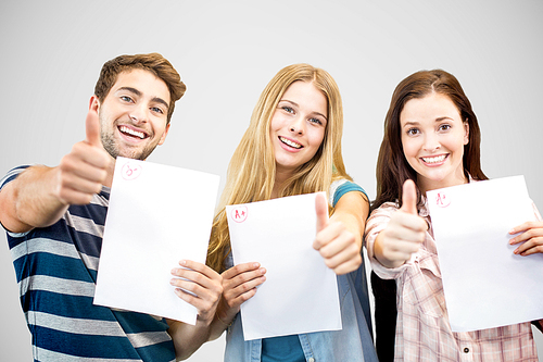 Students holding up exam and doing thumbs up against grey vignette