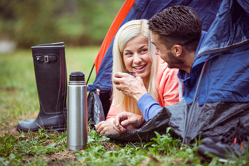 Happy couple lying in tent having hot drinks in the countryside