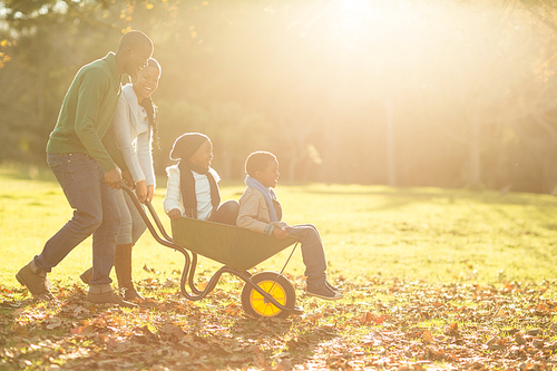 Young parents holding their children in a wheelbarrow on an autumns day