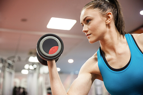 Focused woman lifting dumbbell while sitting down at the gym