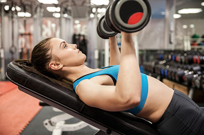 Smiling woman lifting dumbbells while lying down at the gym