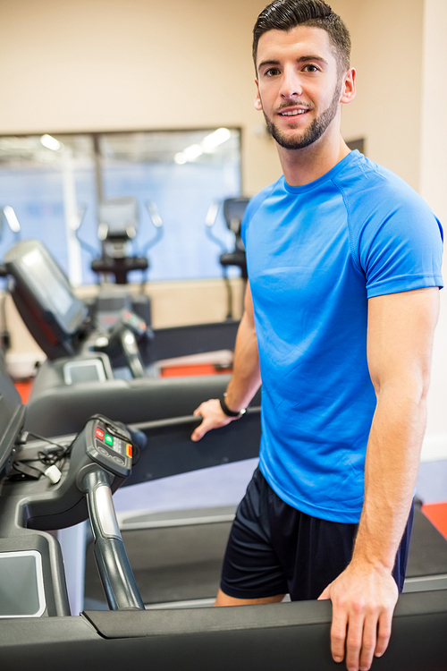 Smiling man standing on a treadmill at the gym