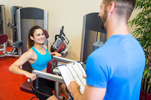 Smiling woman on weights machine beside trainer at the gym