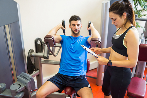 Concentrating man using weights machine with trainer at the gym