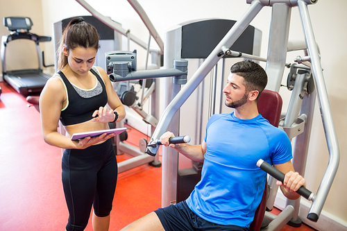 Trainer working with athlete at weights machine at the gym