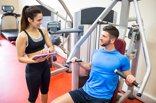 Trainer working with athlete at weights machine at the gym