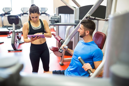 Trainer working with athlete at weights machine at the gym