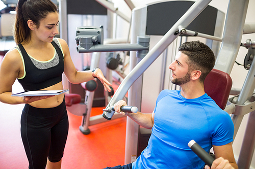 Trainer working with athlete at weights machine at the gym