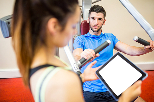 Trainer working with athlete at weights machine at the gym