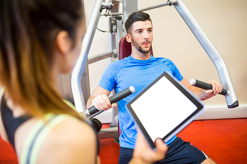 Trainer working with athlete at weights machine at the gym