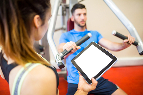 Trainer working with athlete at weights machine at the gym