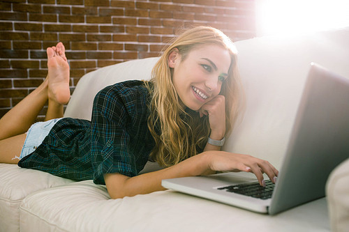 Pretty blonde relaxing on the couch using laptop at home in the living room