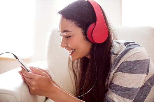 Smiling asian woman on couch listening to music at home in the living room