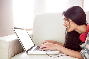 Smiling asian woman on couch using laptop at home in the living room