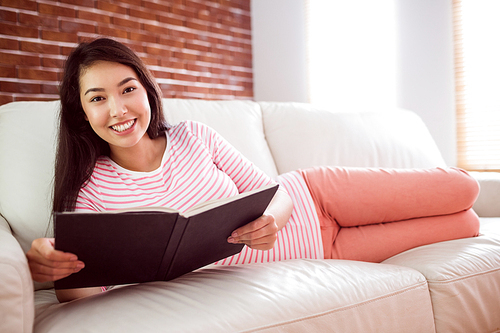 Smiling asian woman on couch reading at home in the living room