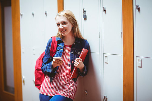 Pretty student with backpack leaning against the locker using smartphone at the university
