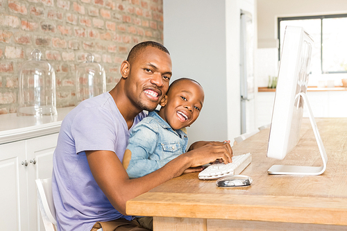 Cute son using laptop at desk with father in living room