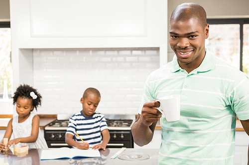 Father drinking hot beverage with children on background in the kitchen